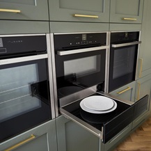 Sage green shaker kitchen with tower wall units, featuring three built in ovens in a row, with a warming drawer pulled out.