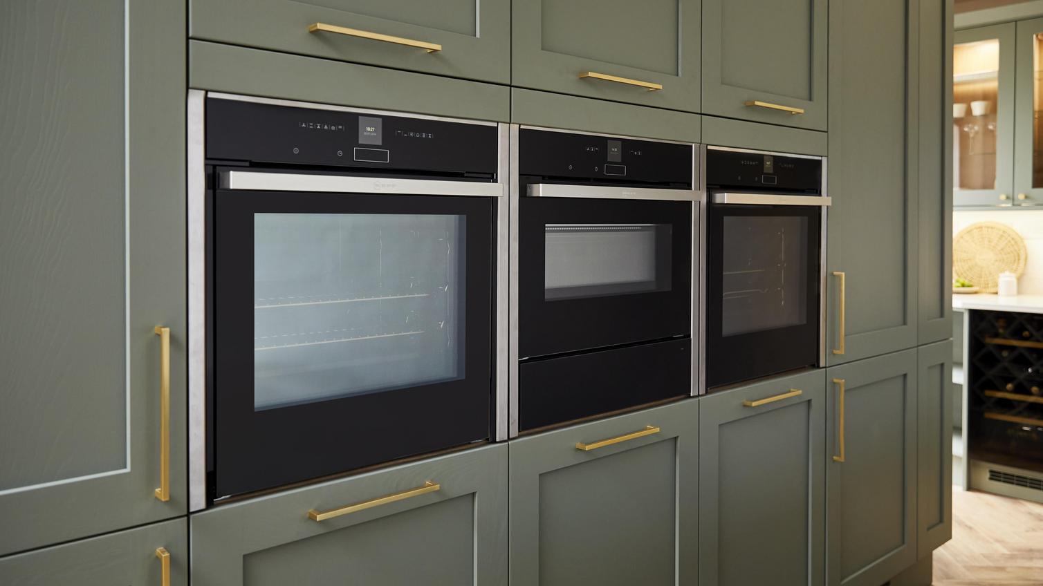 Sage green shaker kitchen with brushed brass bar handles and three built in ovens on tower units.