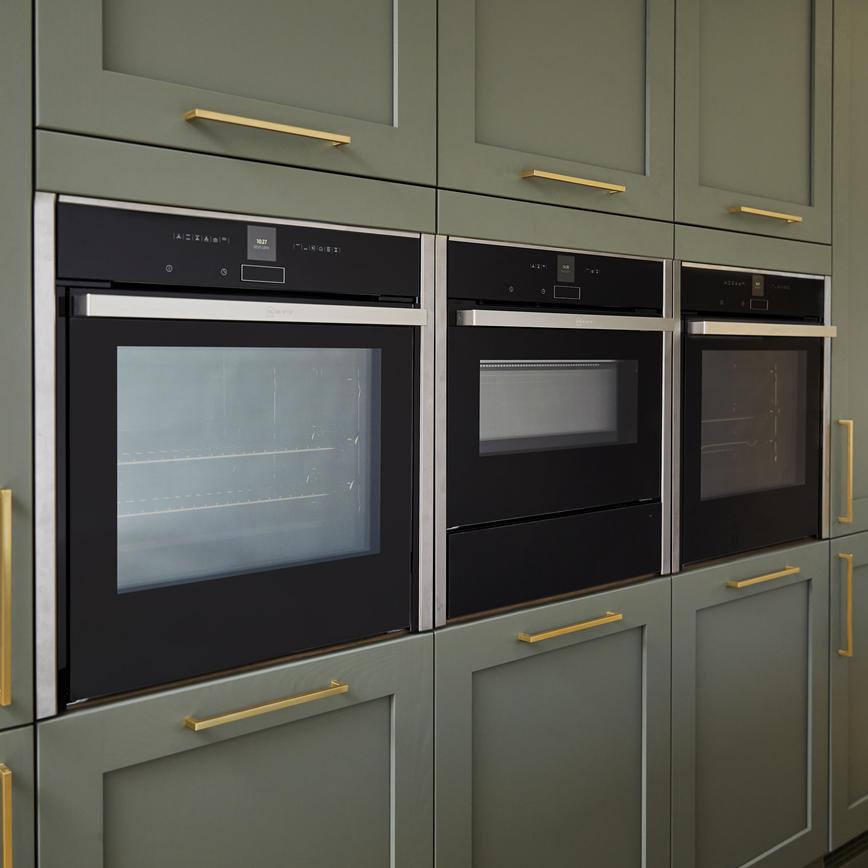 Sage green shaker kitchen with brushed brass bar handles and three built in ovens on tower units.