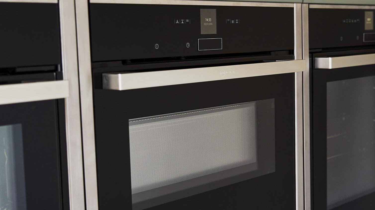 Close up image of built-in steam ovens, three in a row, on a tower unit with sage green shaker doors.
