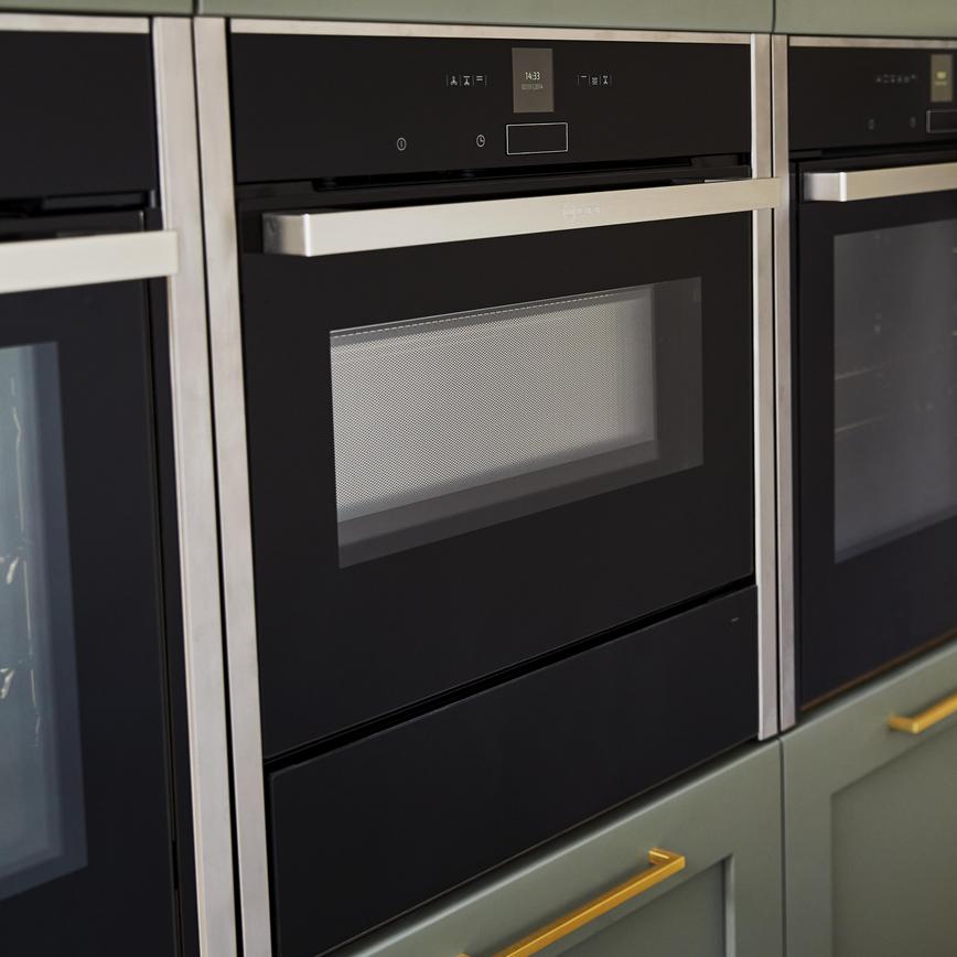 Close up image of built-in steam ovens, three in a row, on a tower unit with sage green shaker doors.