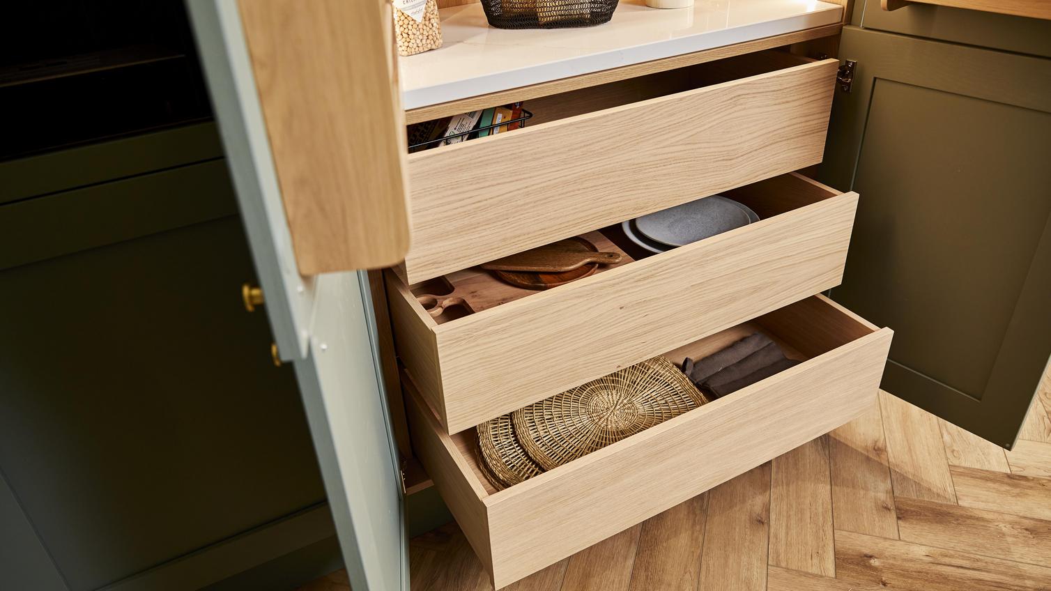 Deep oak internal drawers inside a sage green shaker pantry unit, with place mats and accessories shown in the drawer.