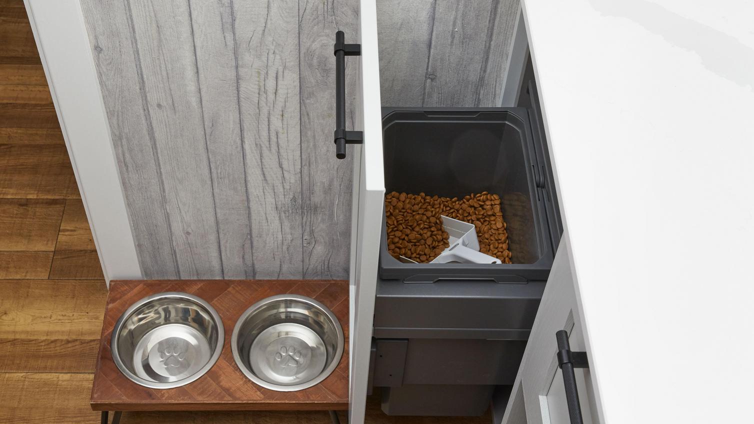 A breakfast bar with an integrated pull-out bin used to store dog food. Also featuring a white, quartz worktop and black handles.