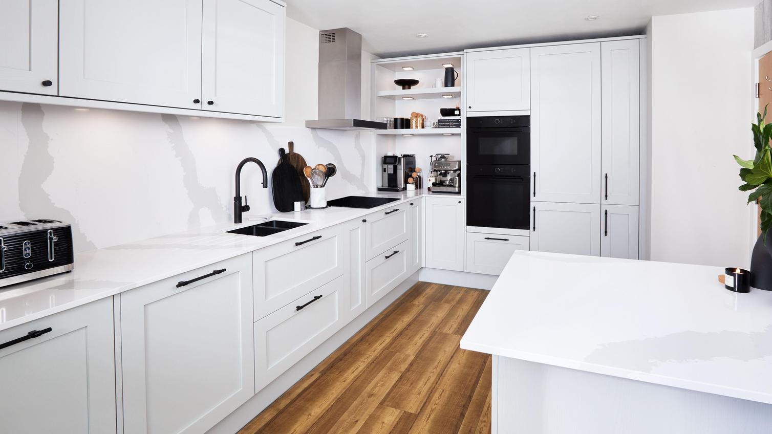 A shaker kitchen with dove-grey doors in an L-shape layout. Includes a black double oven, bespoke shelving, and an inset sink/