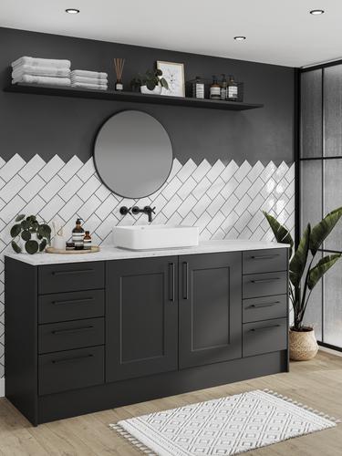 Black shaker cupboard doors in a compact bathroom. Has white metro tiles, a white worktop, a round mirror, and an oak floor.