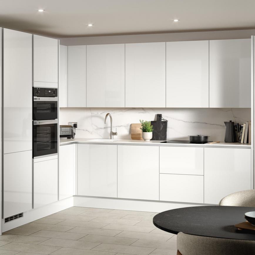 A white, modern kitchen in a gloss finish and handleless cabinets. It is in an l-shaped layout and stone-effect flooring.