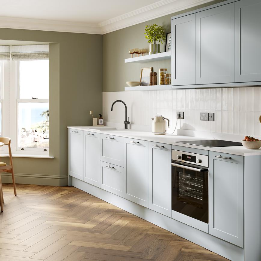 A pale mist-blue shaker kitchen in a single-wall layout. It has matching wall cabinets and dark oak herringbone flooring. 