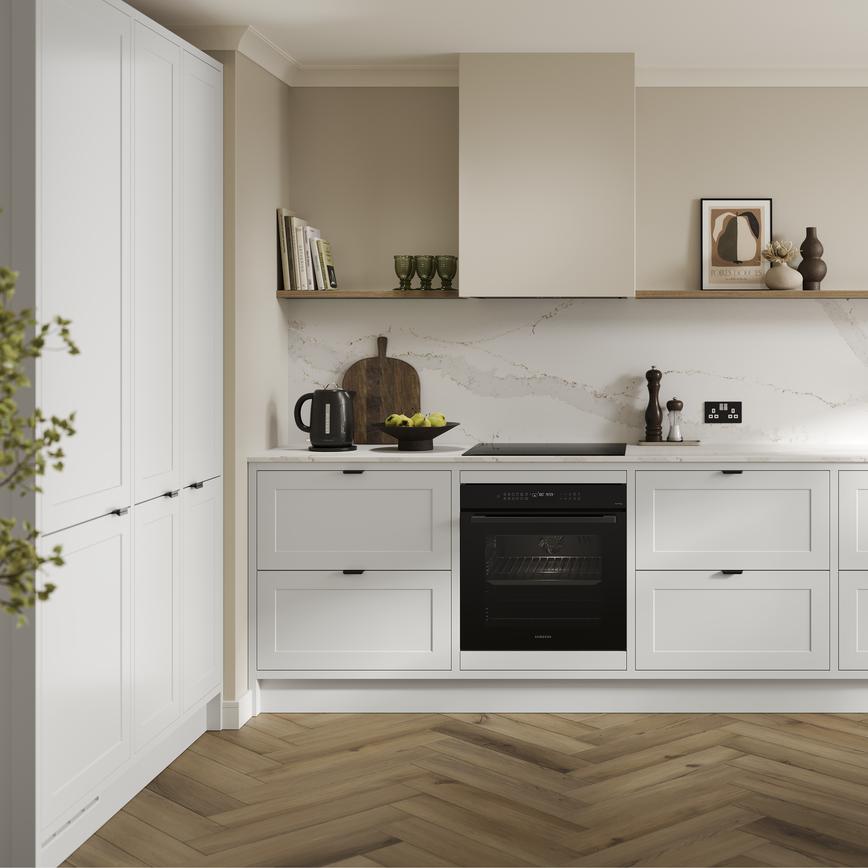 An l-shaped shaker kitchen, in a white colour. It has in-frame detailing with black handles and matching cabinet fixings.