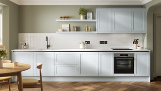 A pale, mist-blue kitchen in a shaker design and handleless style. It has white, natural stone worktops and oak flooring.