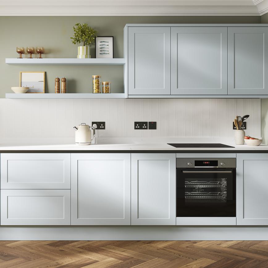 A pale, mist-blue kitchen in a shaker design and handleless style. It has white, natural stone worktops and oak flooring. 