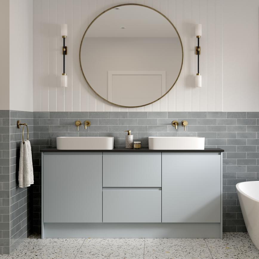 A bathroom in a pale, mist blue tone with large mirror. It has stone-effect flooring, 2-basing setup and brass tap fittings.