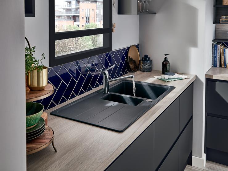 A coordinated black kitchen idea with dark integrated handle doors, a black 1.5 bowl sink, and a navy geometric tile border.