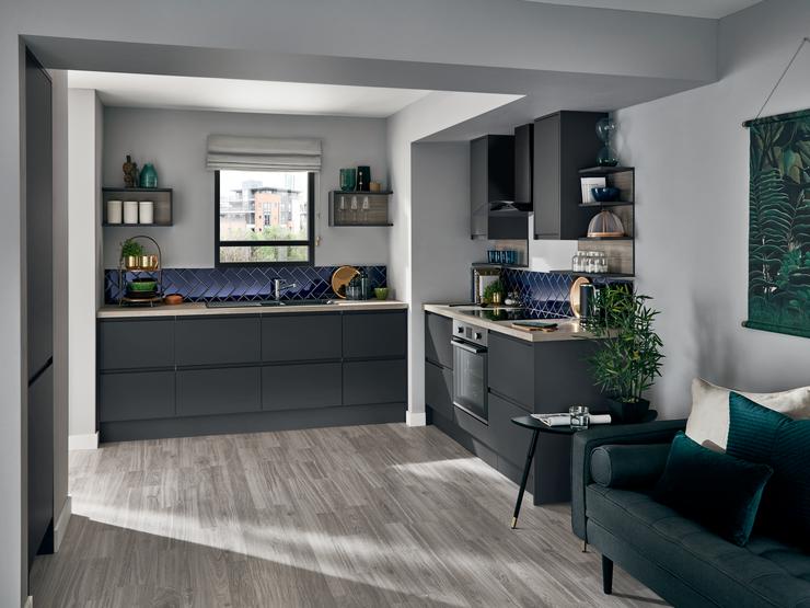 Handleless graphite grey apartment matt kitchen with wood worktop, built under oven and blue diagonal wall tiles.