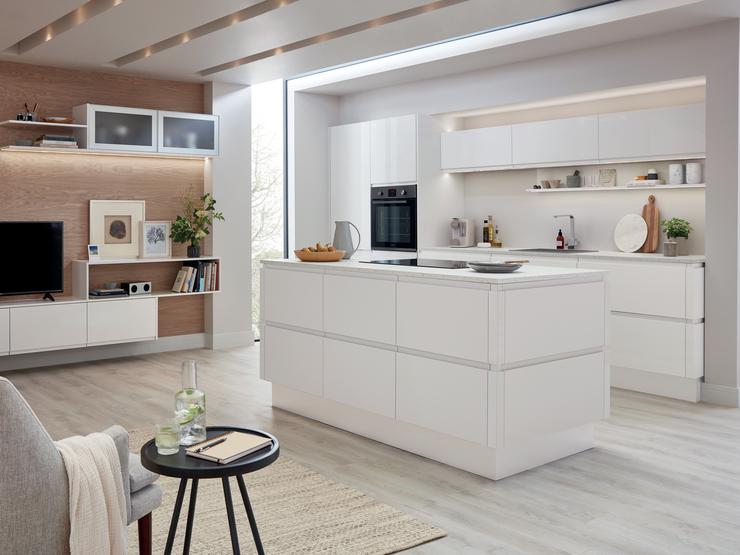 Modern and handleless white gloss kitchen with kitchen island and light oak flooring set in a studio style apartment.