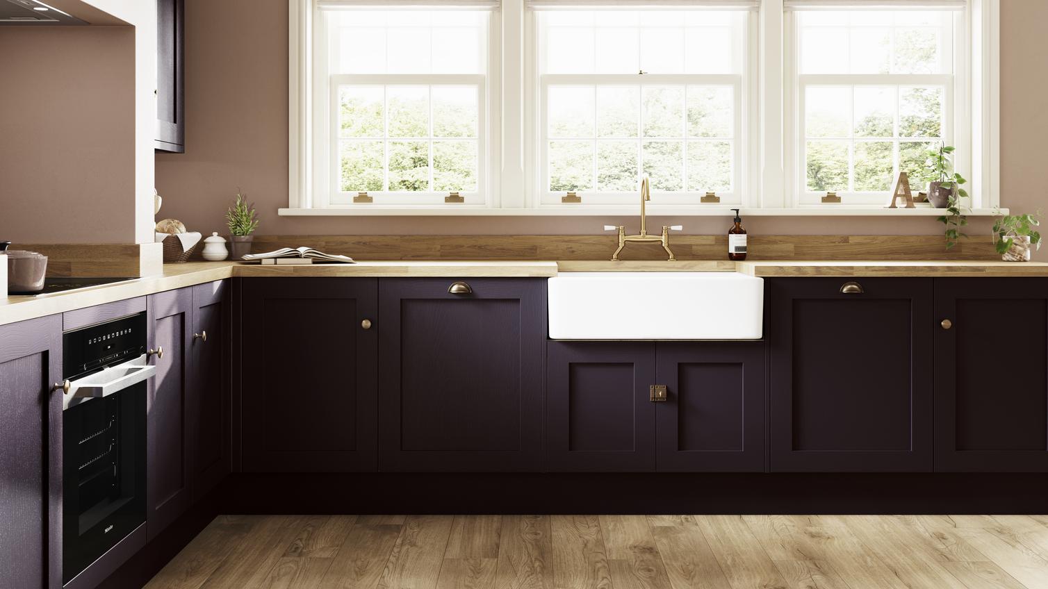 A purple-toned blackberry kitchen in an l-shaped layout. It features oak-effect worktops and brass cabinet accessories.
