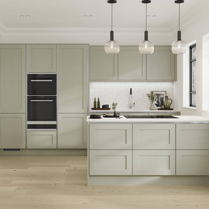 A shaker kitchen with sage-green doors, white worktops, black double oven, and silver profiles for a modern handleless look.