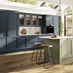 A two-tone kitchen with blue and green shaker doors, white worktops, wooden floors, and brass knobs in a peninsula layout