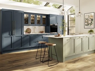 A two-tone kitchen with blue and green shaker doors, white worktops, wooden floors, and brass knobs in a peninsula layout