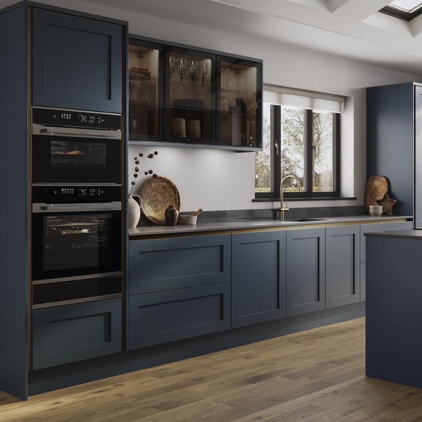 An island kitchen layout with blue shaker doors, black worktops, wood floors, and bronze profiles for a handleless look. 
