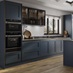 An island kitchen layout with blue shaker doors, black worktops, wood floors, and bronze profiles for a handleless look.