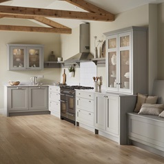 L shape kitchen in pebble grey with shaker style doors. Seated storage bench with cushions and worktop mounted glass cabinet.