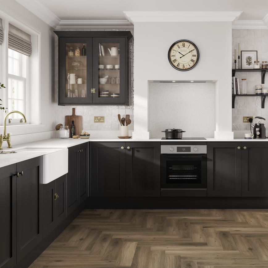 A black shaker kitchen in an L-shaped layout. There are white worktops, chevron oak laminate flooring and a Belfast sink.