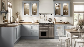 A mist blue shaker kitchen in an L-shaped layout. There are wooden worktops, two glass wall cabinets and a range cooker.