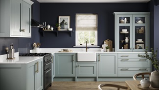 Seafoam blue shaker kitchen in an L-shaped layout. It features white worktops, wall mounted cabinets and brass accessories