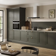 A deep green shaker kitchen with metallic handles. Finished with grey worktop, oak plank flooring, and built-in oven.