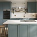 A blue peninsula kitchen with shaker door fronts. The kitchen has marble-effect worktops, breakfast bar, and brass handles.