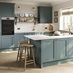 A blue peninsula kitchen with shaker door fronts. The kitchen has marble-effect worktops, breakfast bar, and brass handles.