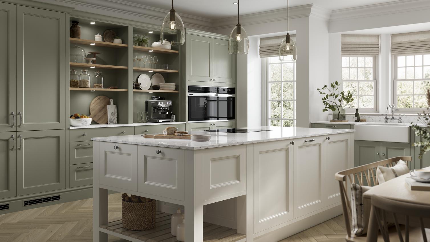 A sage-green shaker kitchen idea with an ivory island. Has white worktops, open shelving, chevron floors, and brass handles.