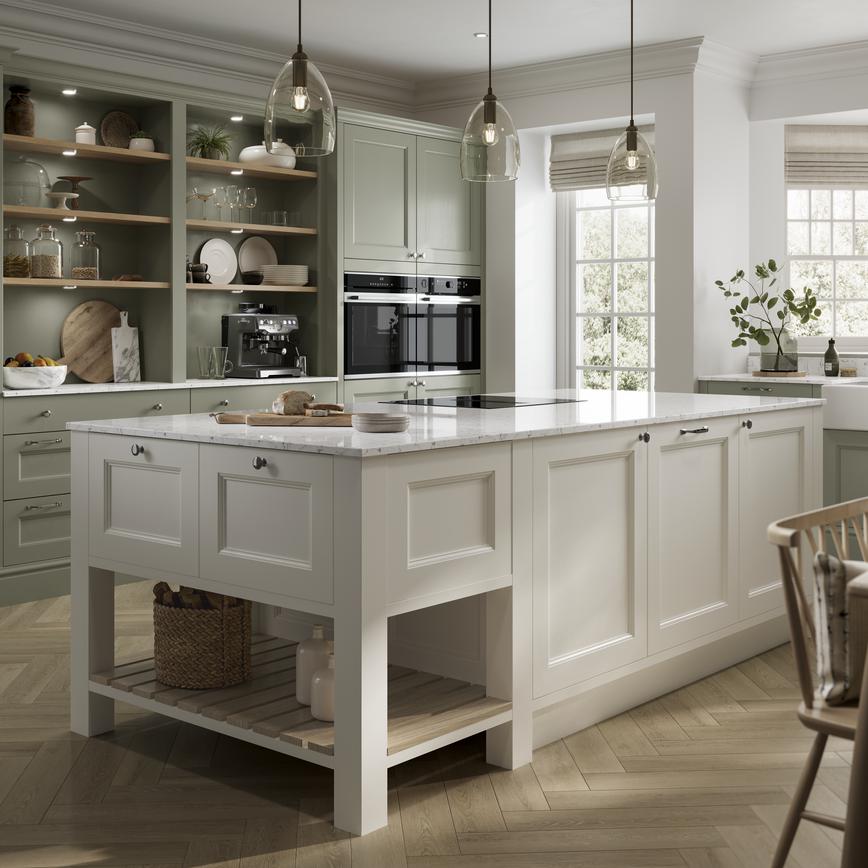 A sage-green shaker kitchen idea with an ivory island. Has white worktops, open shelving, chevron floors, and brass handles.