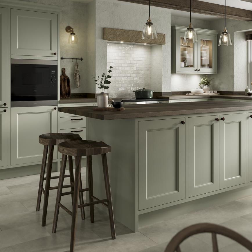 A sage-green in-frame shaker kitchen with an island. Has dark wood worktops, a range cooker, knob handles, and tile floors.
