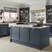 A dark, marine blue shaker kitchen in an L-shaped layout with wood-style worktops. The matching island has white worktops