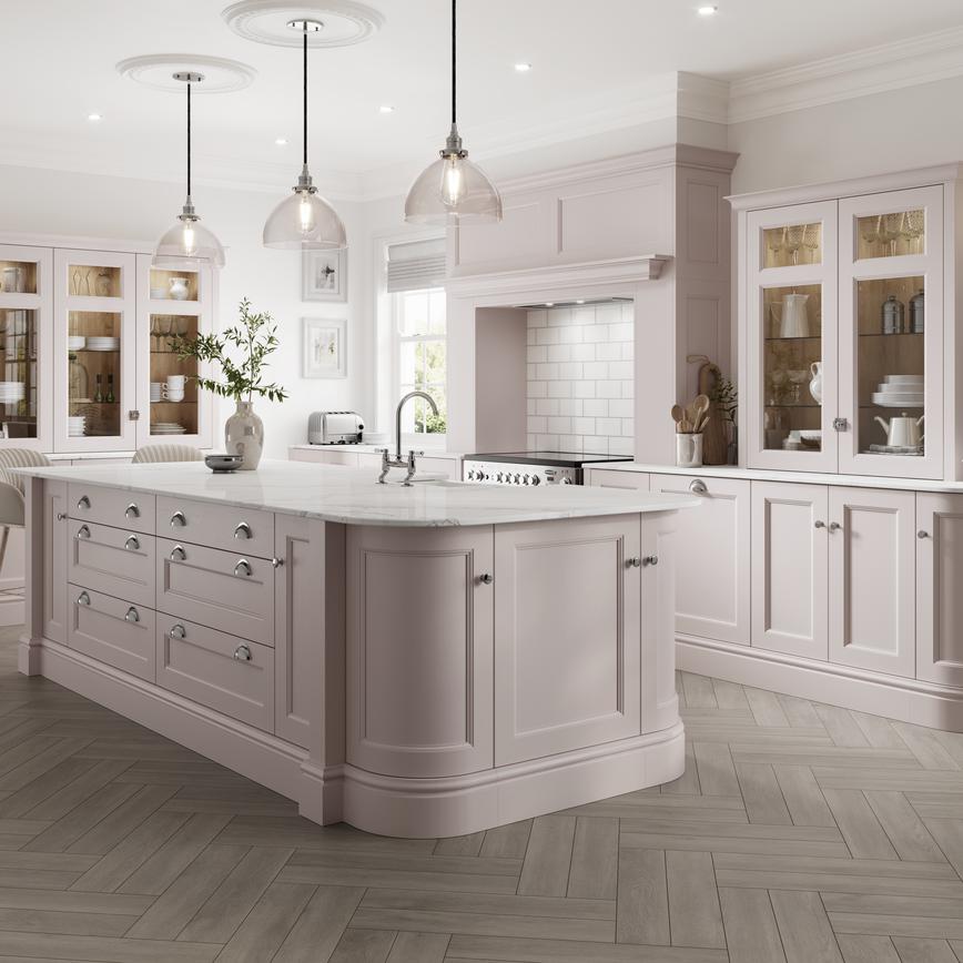 A blossom pink shaker kitchen with a kitchen island and curved corner cabinets. It has a range cooker and white counters.