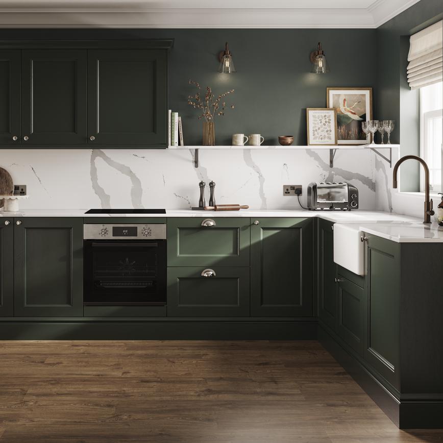 A dark, fir green shaker kitchen in an L-shaped layout. It has white worktops, marble-style backboards, and oak flooring.