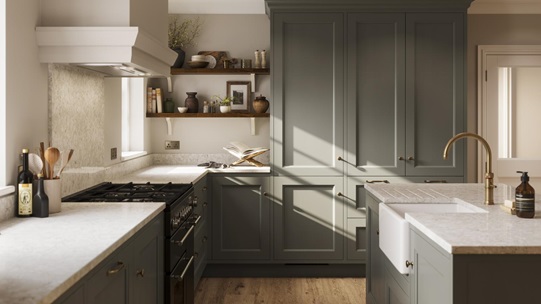 A green kitchen with in-frame, shaker doors in an island layout. It has beige worktops, timber shelving, and plank flooring.