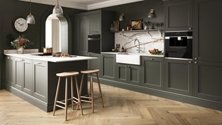 A dark-green kitchen with shaker doors in a single wall layout. It is styled with chevron timber flooring and white worktop.
