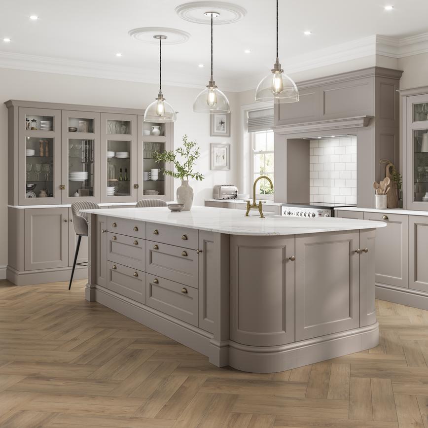 A mushroom-toned, brown kitchen with an island. It has white, bespoke worktop, brass handles, and curved cabinet doors.