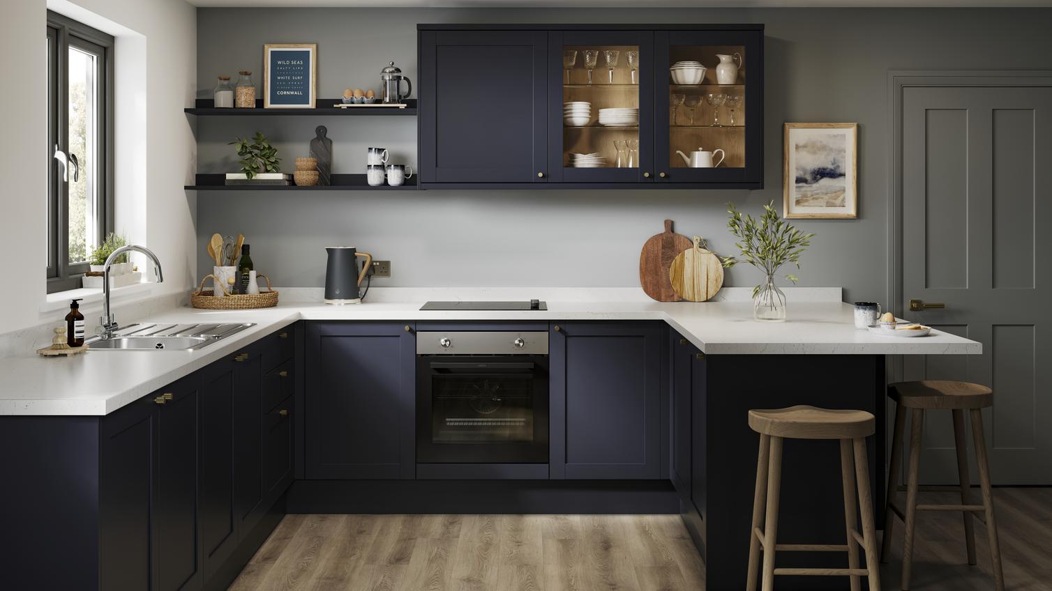 A U-shaped kitchen layout with navy, shaker doors. Includes white worktops, glass wall units, and a black, induction hob. 