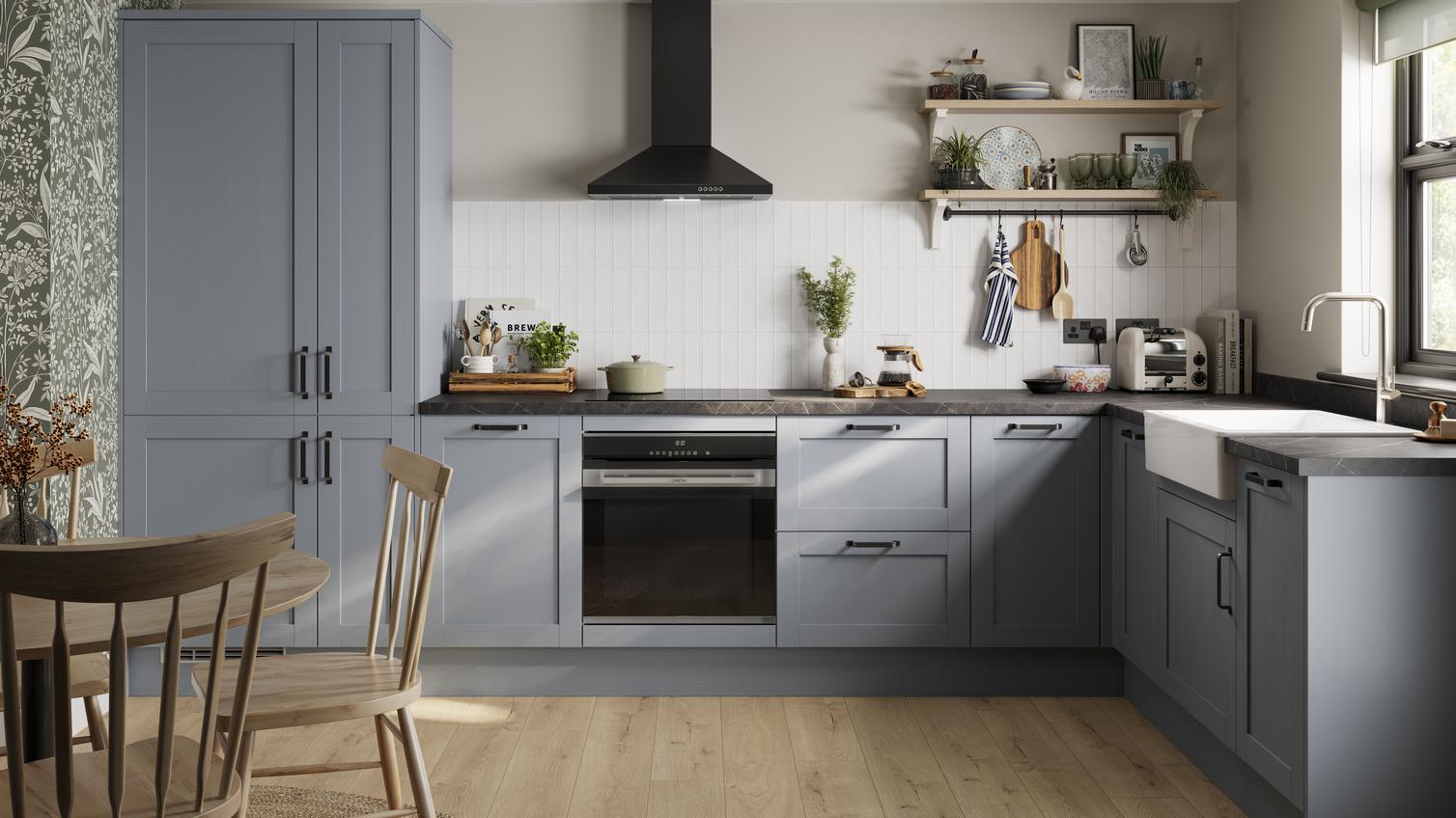 An l-shaped kitchen in a shaker style and dusk blue colour. Features oak-effect flooring and dark stone-style worktops.