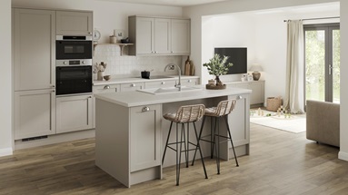 A pebble-coloured shaker kitchen with a single wall layout and a central island. There are white worktops and wood flooring.