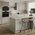 A pebble-coloured shaker kitchen with a single wall layout and a central island. There are white worktops and wood flooring.