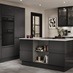 A black, modern kitchen in a gloss finish. It features matching kitchen island, glass wall cabinets, and grey flooring.
