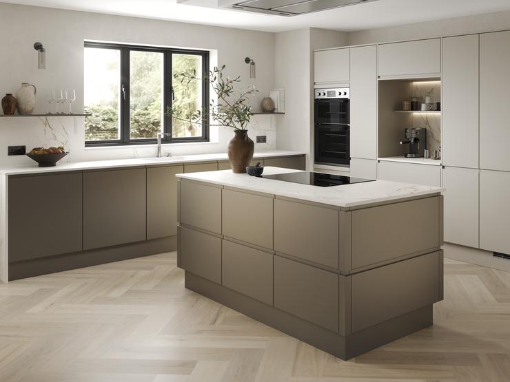 A handleless, bronze kitchen in an L-shaped, island layout. It has white worktops, chevron flooring, and an induction hob.