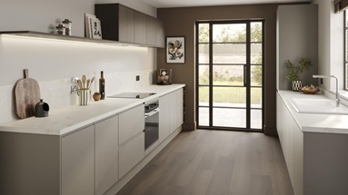 A sand grey, integrated handle kitchen in a galley layout. There are white worktops, white sinks, and dark plank flooring.
