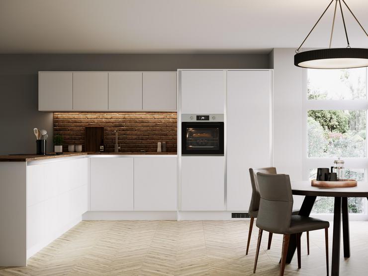 White handleless kitchen in an l shape with brick effect walls, wood worktop, chrome kitchen tap and round dining table.