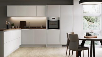 L shape dove grey handleless kitchen with single built in oven and round dining table overlooking mature garden.