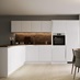 White handleless kitchen in an l shape with brick effect walls, wood worktop, chrome kitchen tap and round dining table.